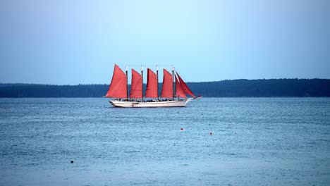 large red multi mast sailboat cruises along blue lake with overcast skies, slow motion