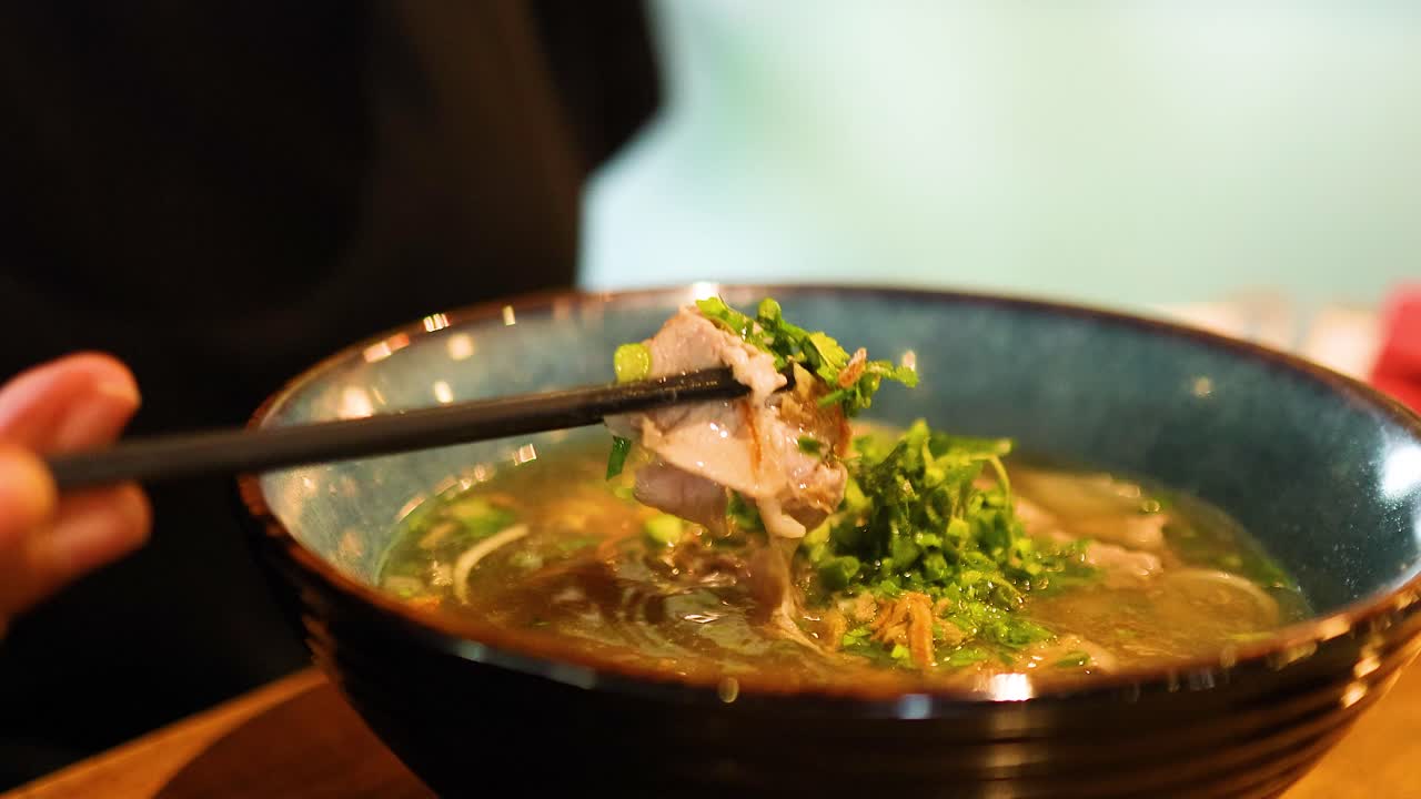 Chopsticks lift noodles from a steaming bowl of pho, highlighting fresh ingredients and warm ambiance