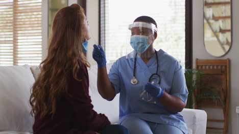 African-american-female-doctor-wearing-face-mask-giving-covid-swab-test-to-female-patient