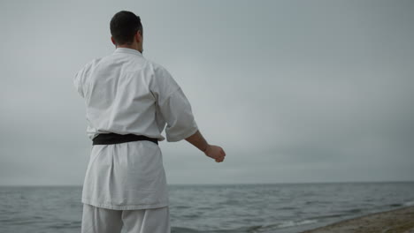 atletas irreconocibles entrenando posiciones de karate en una playa de arena en un día nublado.