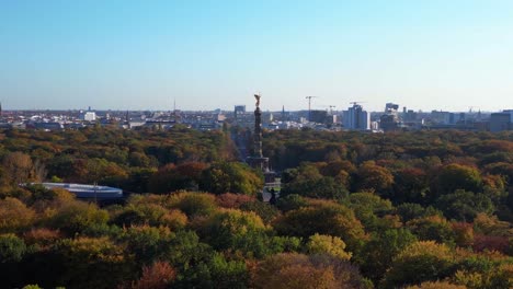 iconic berlin victory column rising above the vibrant autumn foliage of tiergarten park, with the cityscape in the background. smooth aerial view flight wide orbit overview drone