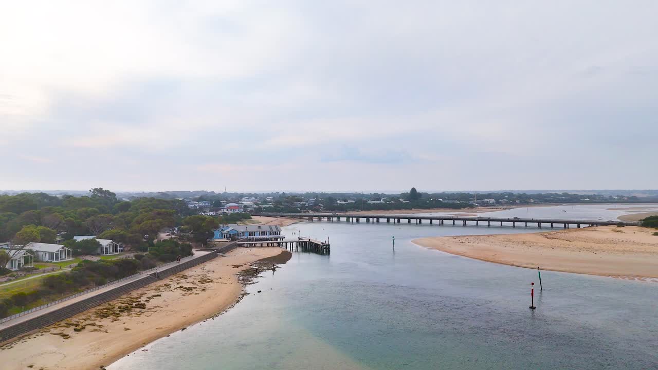 Drone footage captures Barwon Heads' serene coastline and bridge under soft, overcast lighting, showcasing tranquil waters and sandy shores