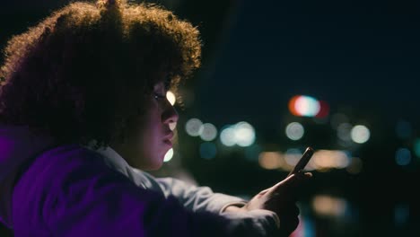 black woman standing on the bridge at night and browsing her mobile phone