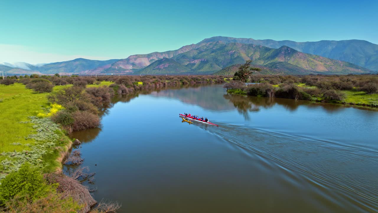 Chilean rowing team practices on a calm river surrounded by scenic mountains and green fields