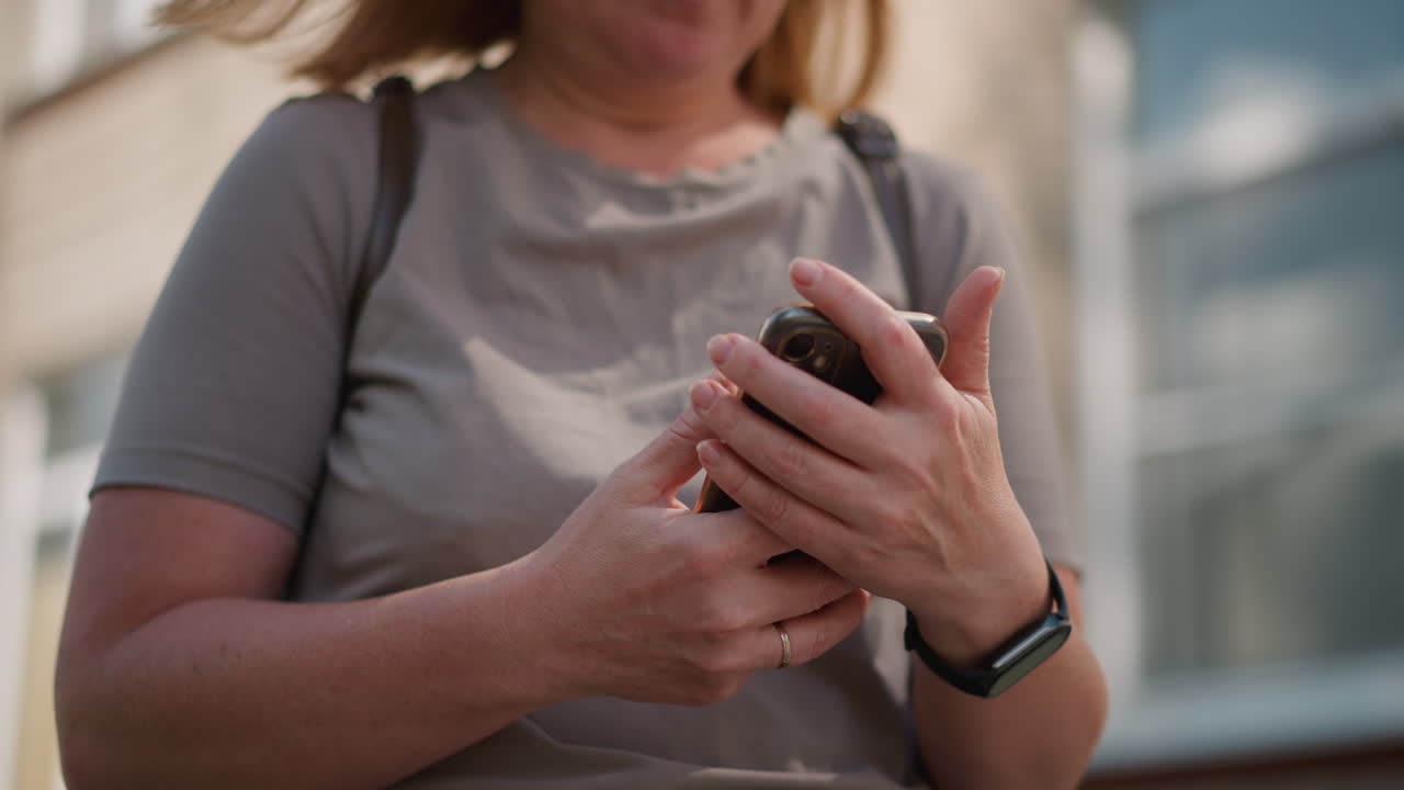 Close up of woman with bag strap holding phone outdoors and pressing it to chest under sunlight, subtle motion capturing emotional moment of hesitation
