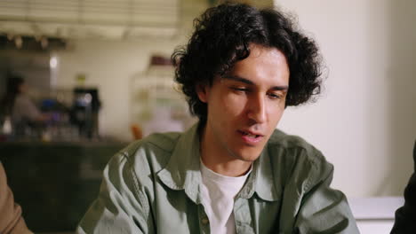 man in green shirt sitting and talking to a group of people