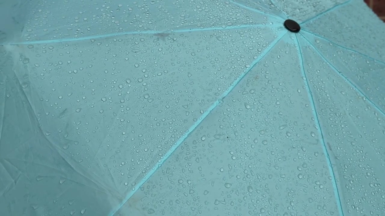 Close up of raindrops on a mint green umbrella in Gosport England