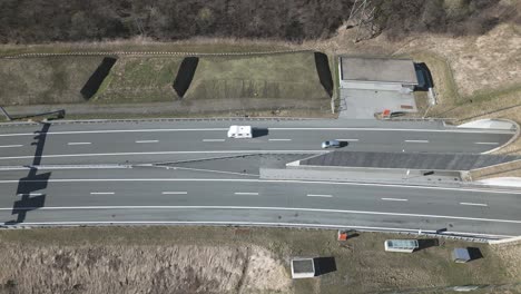 High-Angle-Aerial-View-of-Highway-Traffic-In-and-Out-of-Tunnels-in-Swiss-Alps,-Scenic-Pass-on-Sunny-Spring-Day