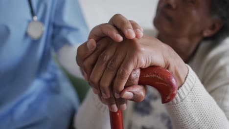 primer plano de una mujer médica africana estadounidense y un paciente mayor tomados de la mano