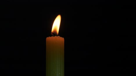 a single candle flickering in a breeze with a black background and close up