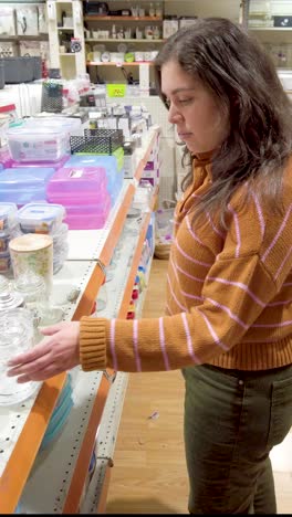 A woman is shopping in a store and is looking at a shelf with glass jars