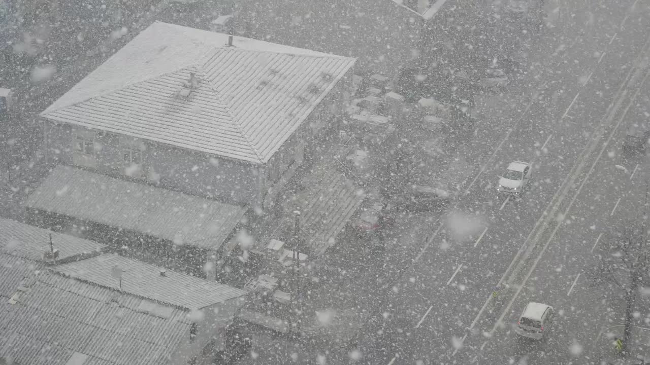 Heavy Snowfall in City with Cars and Buildings from Above