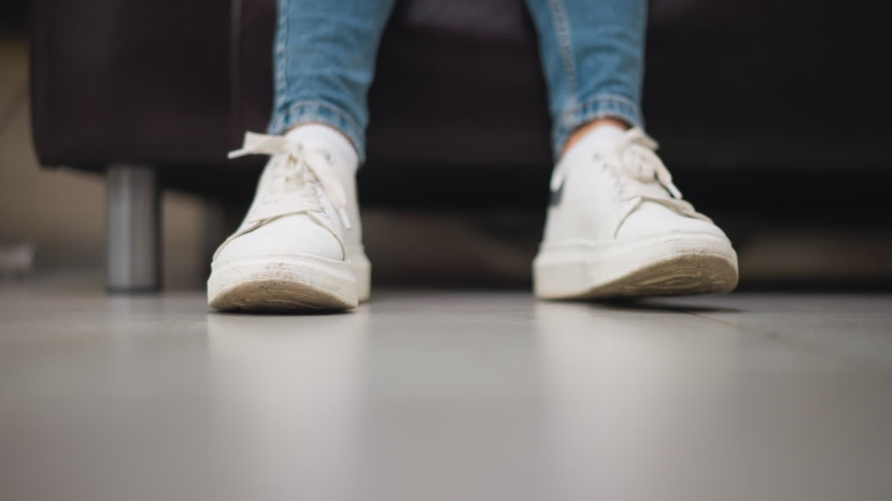 타일로 된 바닥에  스니커의 클로즈업, 다리가 약간 교차되어, 캐주얼 스타일과 움직임을 보여주는, 흐릿한 배경으로 부드럽게 발을 는