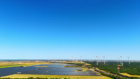 approaching fields covered with multiple solar panels. wind farms nearby produce green energy. aerial view