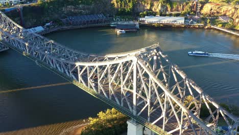 Vista-Aérea-De-Pájaros-Drone-Que-Captura-El-Tráfico-De-Vehículos-Ocupados-Cruzando-El-Río-En-El-Icónico-Puente-Histórico-De-La-Historia-Al-Atardecer-En-Las-Horas-Doradas,-Ciudad-De-Brisbane,-Queensland