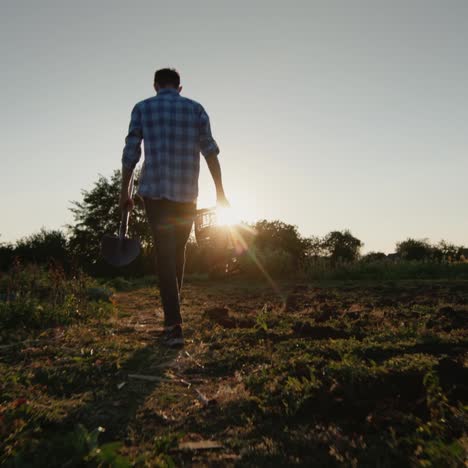 un granjero con una pala y una caja vacía camina por su campo al sol 1