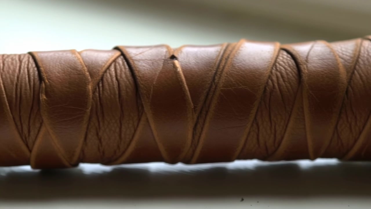 Close-up view of a brown leather binding coil showing stitching and textured grain, captured in a warm crafts environment; mid sequence frame from a short