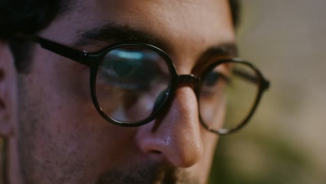 close-up of a man wearing glasses, working on a computer at night.