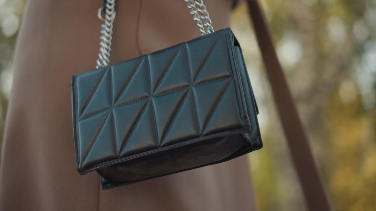 Primo piano di una borsa in pelle trapuntata nera con tracolla a catena argentata appesa alla spalla, che mostra i dettagli della texture e le cuciture. La borsa rimane il fulcro principale, enfatizzando i suoi elementi di design.