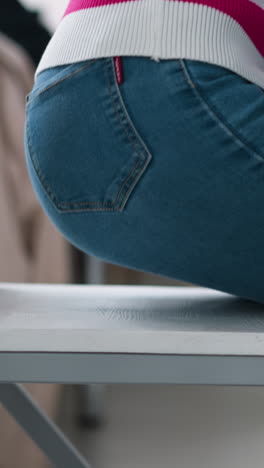 woman sits down on chair at table closeup. slim lady in jeans uses minimal wooden seat to rest at round desk. simple furniture for home interior