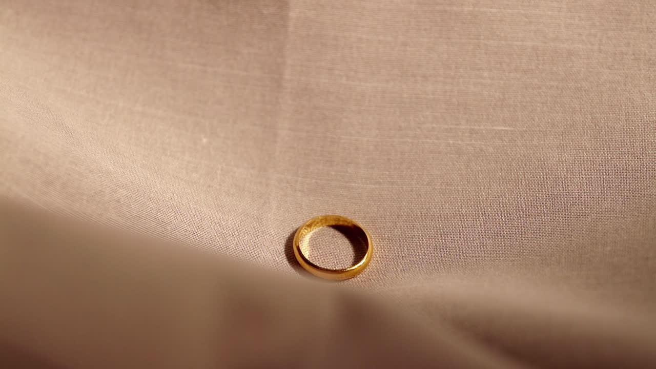 Single gold engagement ring sliding downwards over a tan-colored cotton fabric