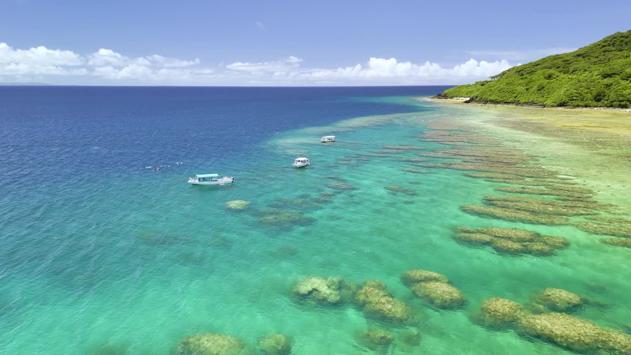 Splendida ripresa con drone di barche con fondo di vetro che galleggiano su vivaci formazioni coralline nelle acque turchesi dell'isola di Ishigaki, Giappone.
