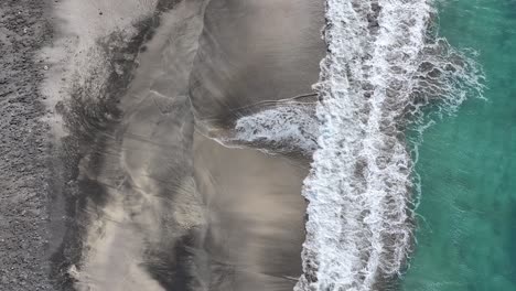 Birdseye-Aerial-View-of-Ocean-Waves-Breaking-on-Empty-Sandy-Beach-of-Volcanic-Island-60fps