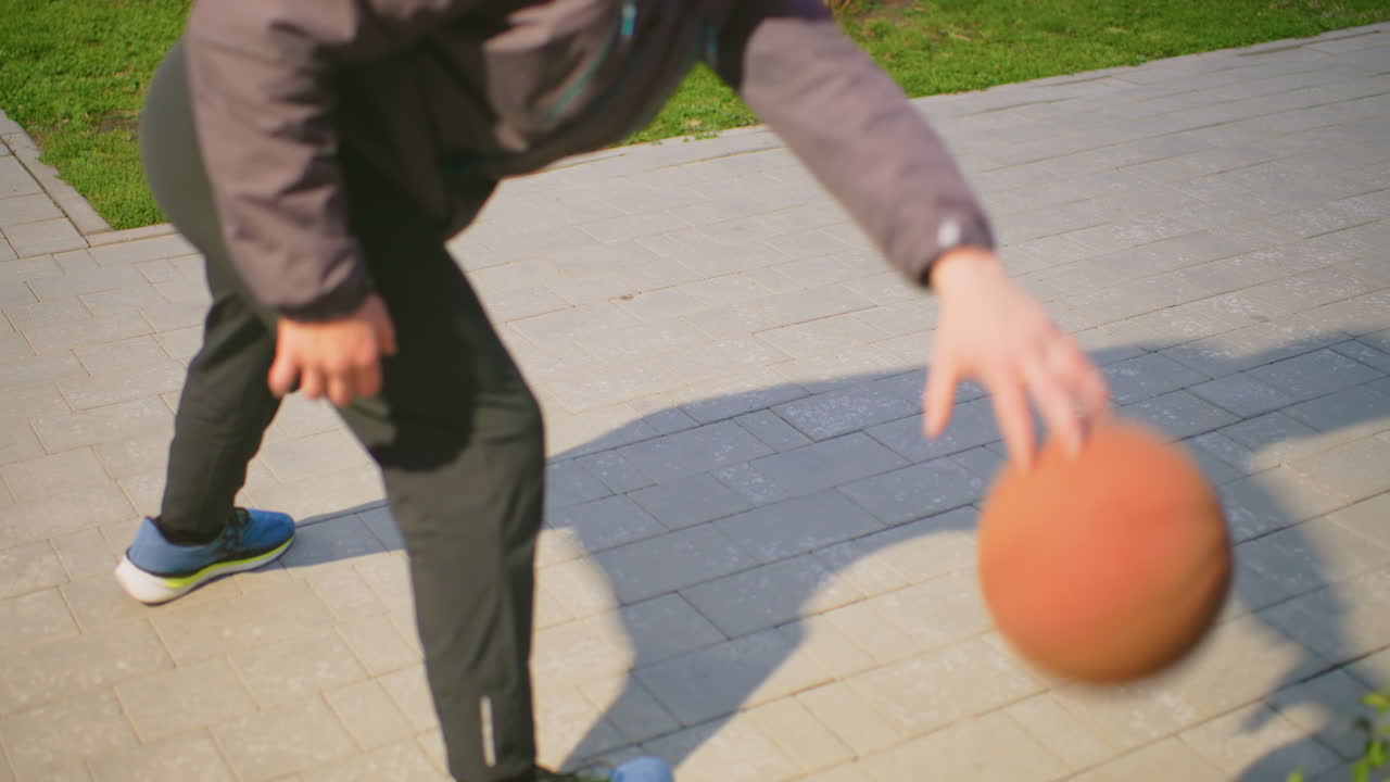 Young athlete practicing ball handling outdoors, Individual honing dribbling skills under sunlight on pavement, Person performing quick footwork drills with basketball in sunny park setting