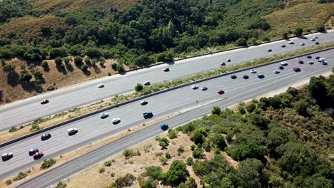 Vista-Aérea-De-Pájaro-Del-Tráfico-Ligero-De-La-Tarde-En-La-Autopista-De-California-Con-árboles-Y-Follaje-En-Ambos-Lados