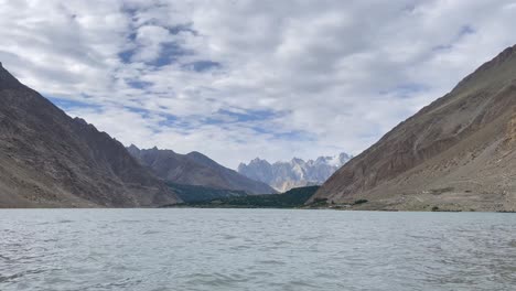 a tranquil scene of attabad lake surrounded by majestic mountains in the gojal region of gilgit-baltistan, pakistan, under a partially cloudy sky.