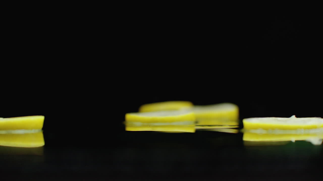 맛있는 프레트 슬라이스는 반사 및 스프레이와 함께 테이블에 떨어집니다. 노란색 익은 레몬의 반지의 느린 움직임.