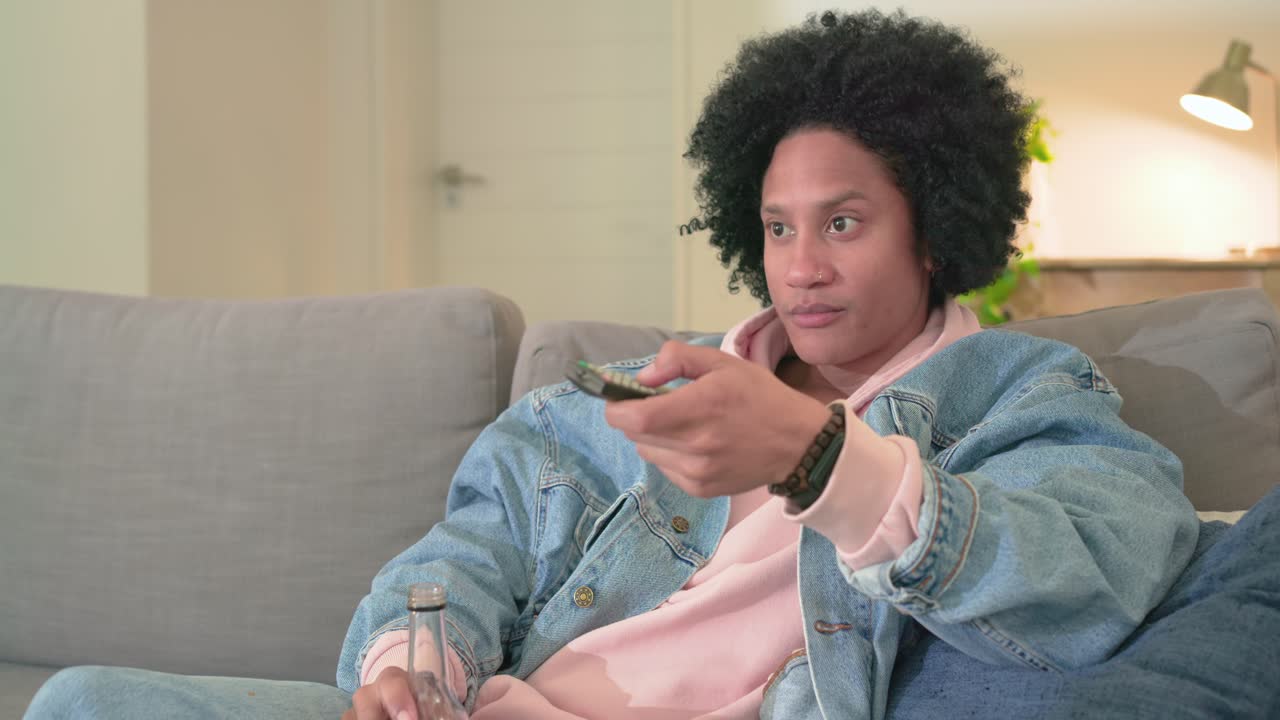 La TV cambia, uomo afroamericano preme il telecomando, sorseggia una bevanda rossa sul divano a casa, spazio per il testo