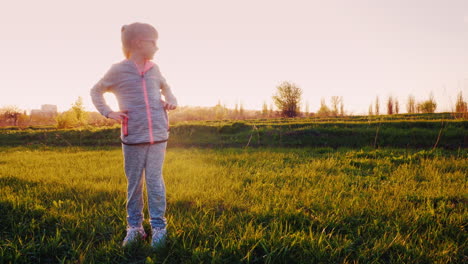 A-6-Year-Old-Girl-Is-Doing-Exercises-On-A-Green-Meadow-At-Sunset-1