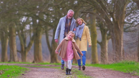 grandparents watching granddaughter skipping ahead on outside walking through winter countryside