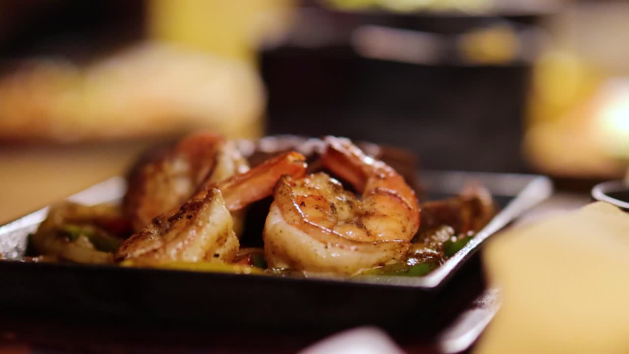 Close-up of sizzling shrimp and beef fajitas on a hot plate, captured in a warm, inviting restaurant ambiance