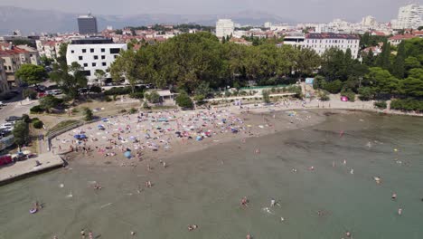 Aerial:-Bacvice-Beach,-Split,-Croatia-with-sunbathers-and-city-backdrop