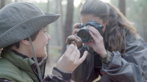 Cerca-De-Una-Madre-Feliz-Tomando-Una-Foto-De-Su-Hijo-Sosteniendo-Hongos-En-El-Bosque