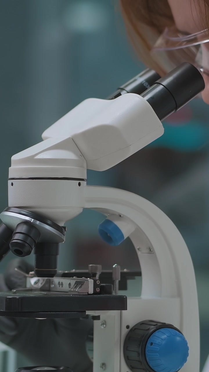 Scientist Adjusting and Looking Through a Microscope in a Laboratory