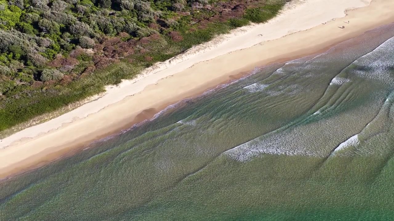 High-angle aerial shot of ocean waves rolling onto a sandy beach in New South Wales.