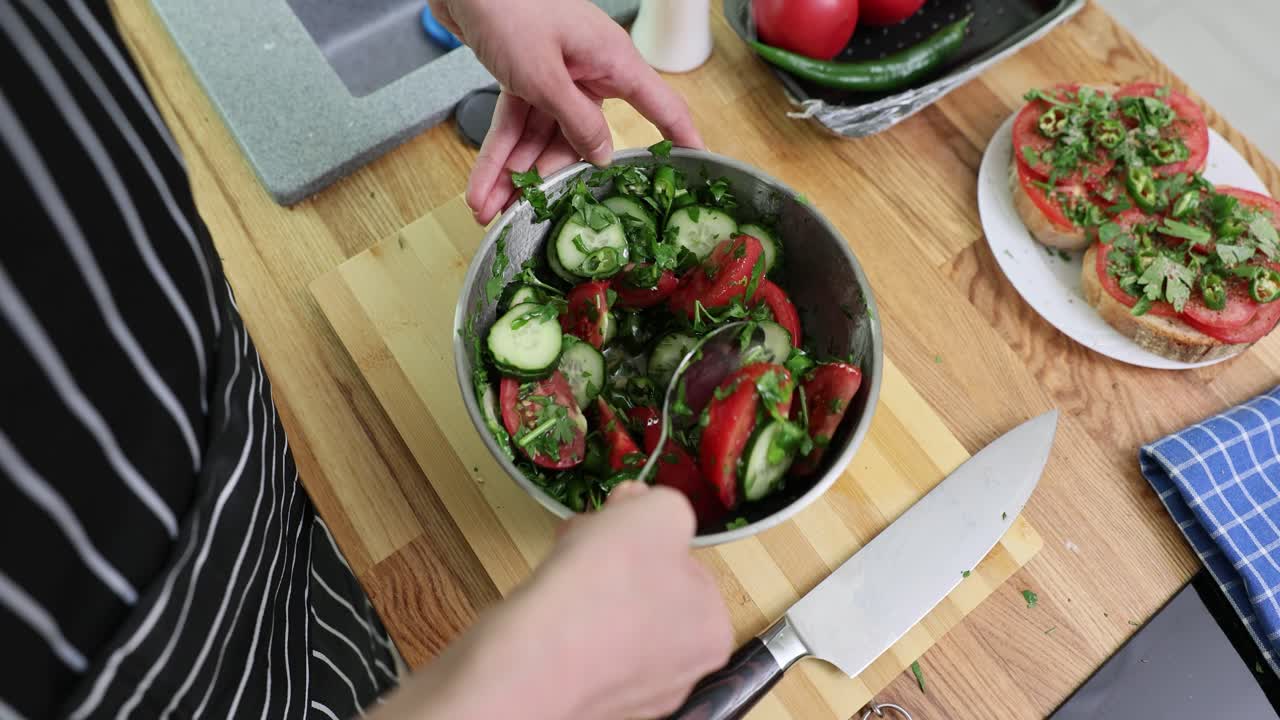 Hands mixing a fresh tomato and cucumber salad in a kitchen