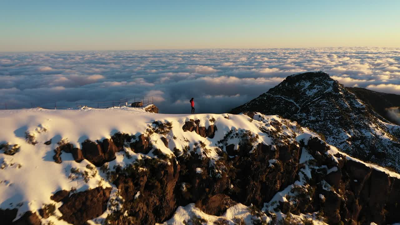 mujer sola disfrutando del paisaje épico desde la cima de la montaña pico ruivo en madeira con un lecho de nubes detrás de ella