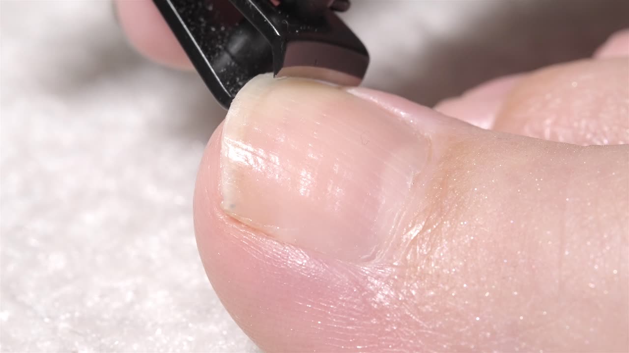 Detailed 4K close-up of woman trimming her big toenail using a black nail clipper
