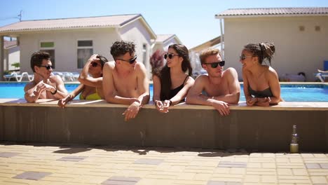 Young-attractive-people-hanging-out-at-the-side-of-the-pool-in-the-summertime.-Pool-party.-Slow-Motion-shot
