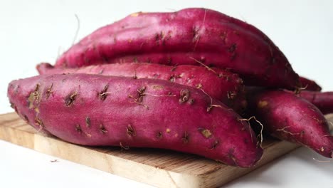 close up of raw sweet potato on chopping board on white background