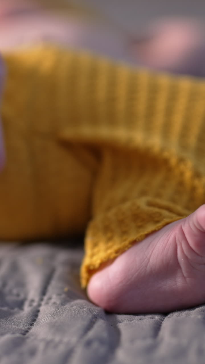 Small kid in yellow pants lying on the bed with his tiny feet to the camera. Beautiful little baby feet close up. Vertical video