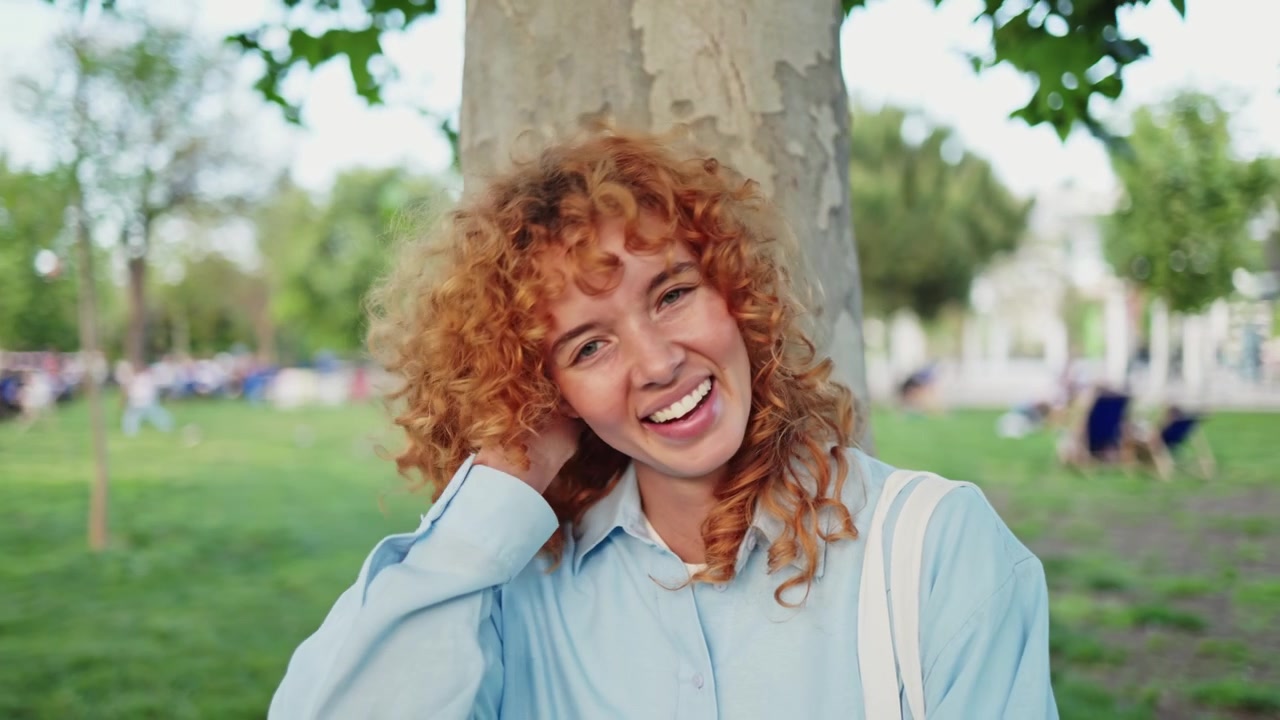 Ritratto di una giovane donna sorridente con capelli rossi ricci in un parco