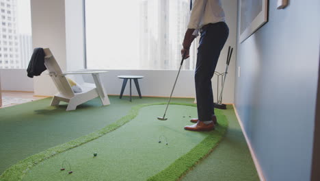 businessman practicing golf on indoor putting surface in office