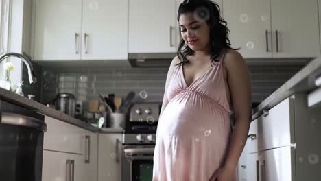 a serene moment in the kitchen: expecting mother embracing pregnancy glow in soft lighting and comfortable attire, surrounded by gentle bubbles for a joyful atmosphere