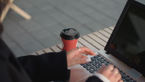 close-up of laptop on table with visible keyboard. person holding tea cup next to laptop, dropping it on table, and starting to type, fingers adorned with rings, reflection of cup and hand on screen