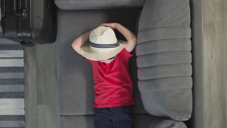 stylish small boy puts hands behind head lying on sofa